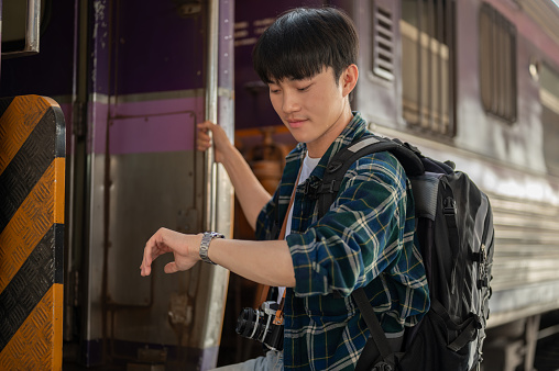 A handsome young Asian man traveler is checking time on his wristwatch while getting off the train, checking the arrival time.