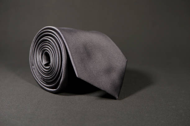 istock Plain black color necktie rolled on black surface with black background close-up view single object 1926371299