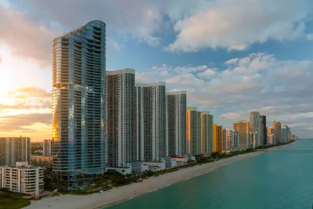 Photo of Aerial view of Sunny Isles Beach city with luxurious highrise hotels and condos on Atlantic ocean shore at sunset. American tourism infrastructure in southern Florida