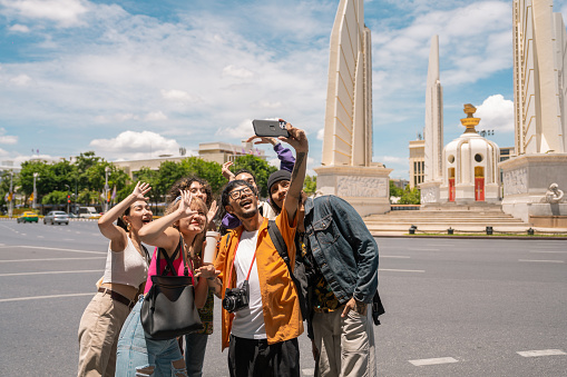 Group of cheerful young Asian man and woman taking selfie with smartphone while  a traveling Vibrant Streets and Cultural Wonders in bangkok