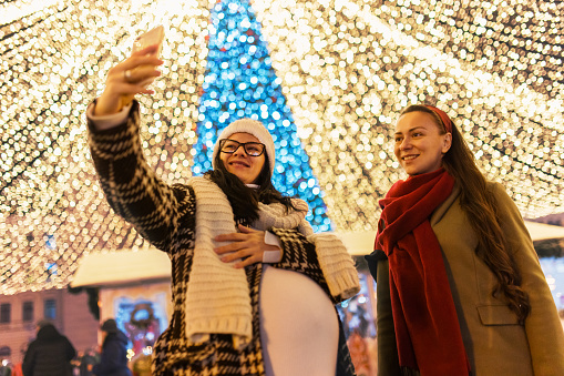a young pregnant woman and her friend are walking around the square at night -christmas market