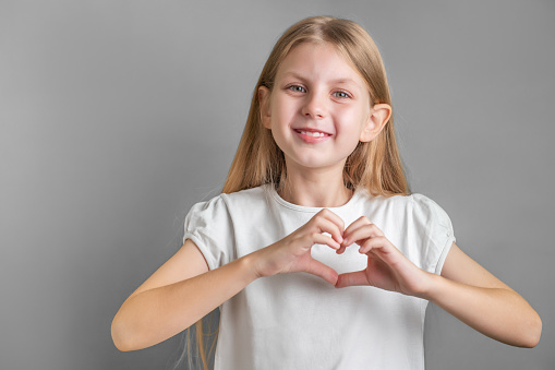 Cute little girl with long blonde hair showing heart sign