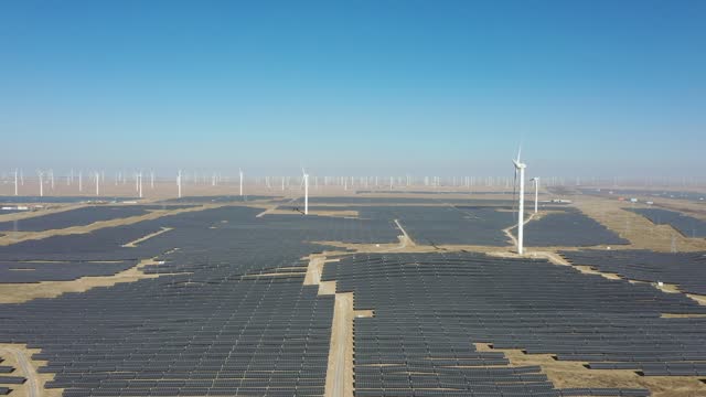 High-angle bird's-eye view of solar photovoltaic panels and wind turbines in the desert