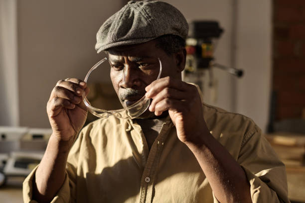 Portrait of African American senior carpenter putting on protective glasses in sunlit workshop