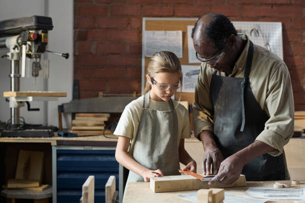 istock Girl Measuring Wood in Workshop Studio with Senior Carpenter Helping 1926653905
