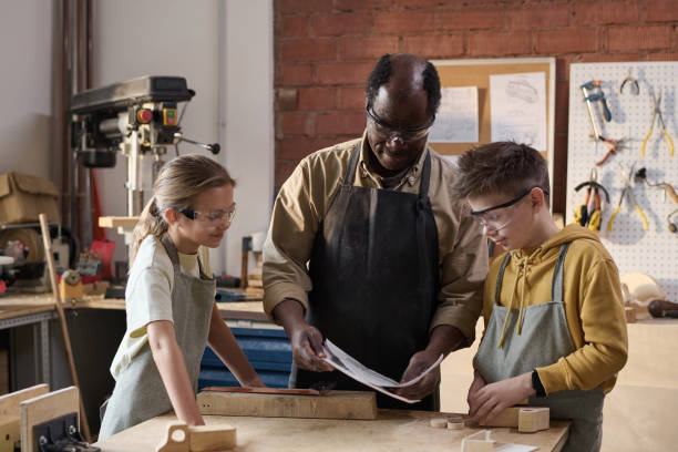 istock Senior Black Man Working on Carpentry Project with Smiling Children in Workshop 1926654448