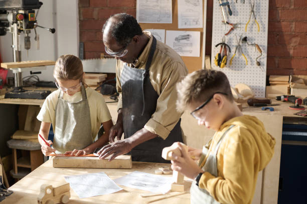 istock Senior Carpenter Teaching Children Carpentry in Workshop 1926654963