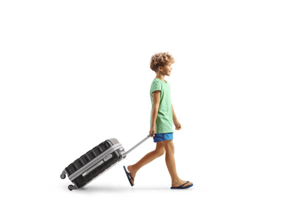 Full length profile shot of a boy walking and pulling a suitcase isolated on white background