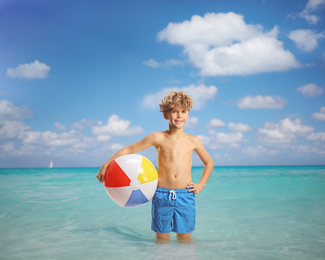 Boy standing in the sea and holding a beach ball