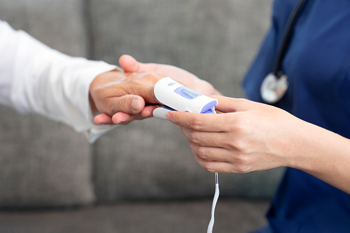 young asian female nurse measuring pulse with oximeter to a senior woman at home,concept of elderly people health care,homecare,home health nursing