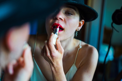 Young woman painting her lips in the mirror wearing an elegant hat