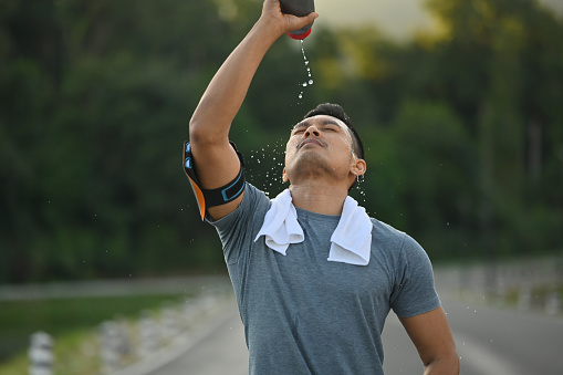 Sporty man pouring water over his face to refresh after after training hard outdoor.