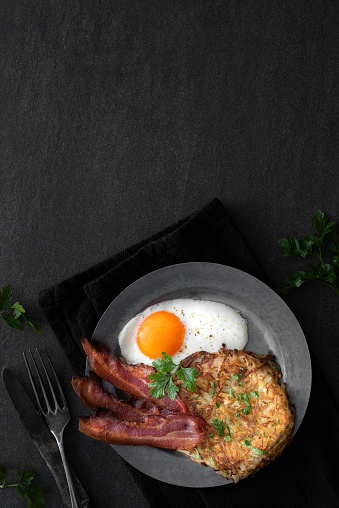 Homemade Hash browns with fried bacon and  egg on a dark background