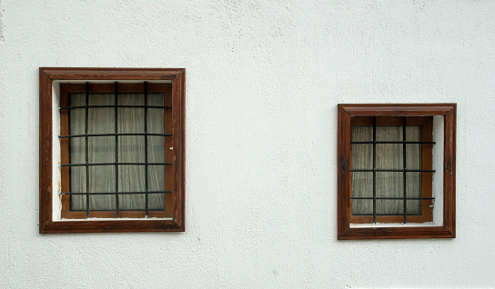 Two old wooden windows  with metal grill of different sizes on facade