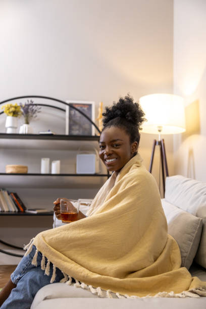 istock Smiling woman drinking tea while sitting on sofa wrapped in yellow plaid in home interior 1926860161
