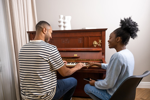 Adult man sitting at piano having musical lesson from female teacher at home