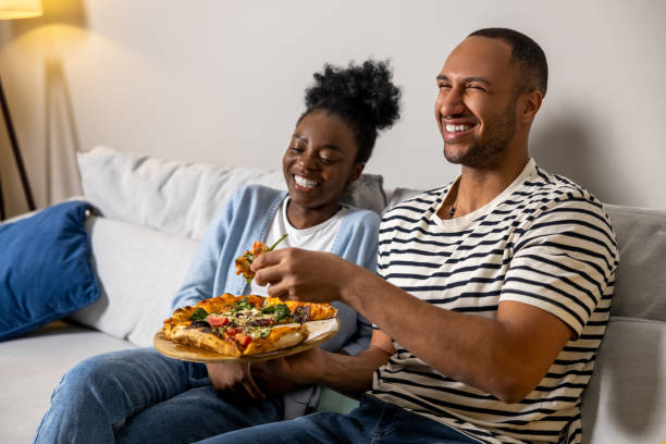 istock Couple eating pizza snack at home and laughing while resting on sofa 1926860741