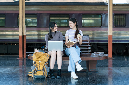 Woman traveler with backpack using laptop to planning vacation on holiday relaxation at the train station.