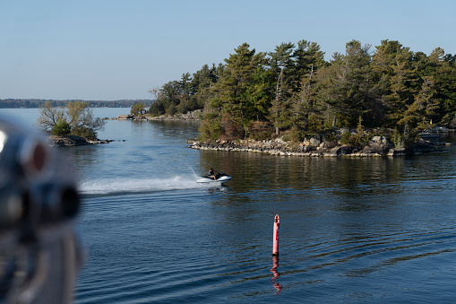 One of the thousand islands near Gananoque on Lake Ontario.  There is a jet skier beside the tour boat.