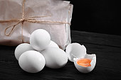 Fresh chicken white eggs with hay on sack and rustic wood, organic farming on black background. Healthy natural food
