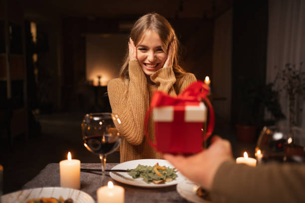 istock Beautiful loving couple is spending time together at home or restaurant. Man present gift box his wife and having romantic dinner. Celebrating saint valentine's day concept. 1926891205