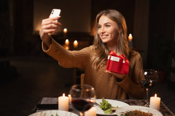 istock Romantic dinner at home or in a restaurant. Celebrating Valentine's Day. A young woman taking a selfie with a gift sits alone at a festive table on a romantic evening 1926891718