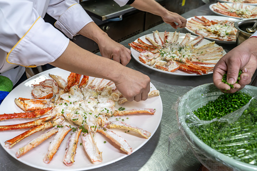 The chef's hand is adding seasoning to the cooked king crab