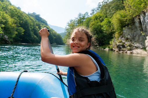 Portrait of a happy girl paddles while sitting in a boat during rafting on the river