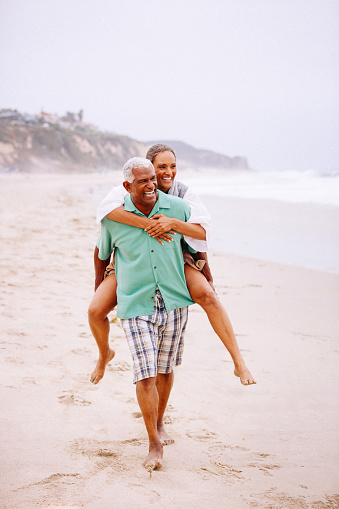 Senior African American couple having fun piggybacking at beach.