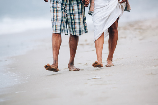 Legs of senior African American couple walking with at sandy beach. Model released.