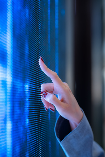Vertical image of Focus woman hand pointing at blue digital screen with blur face background and blue light of technology.