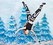 Smiling girl is flying upside and waving hands on blue background with fake spruce trees