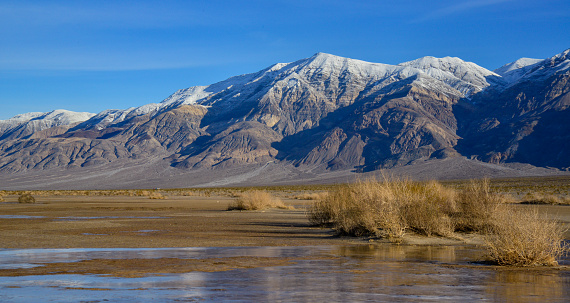 Landscape of wet clay desert in winter against the backdrop of snow-capped mountains in the Death Valley area, California