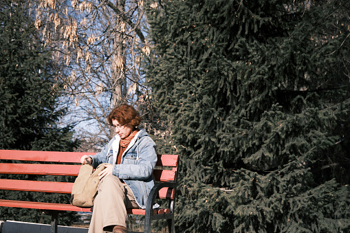 Single mature woman is sitting on park bench