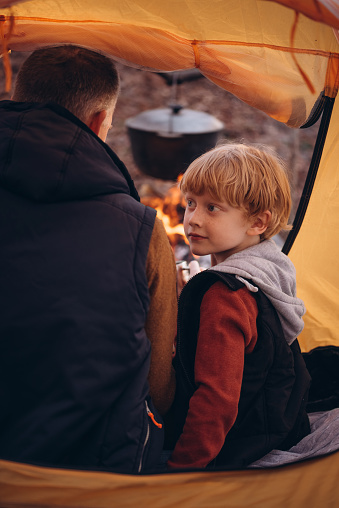 Man and boy tourists autumn time leisure, vacation hiking or traveling touristic activity. Family camping, father and little son relax in forest camp at fire.