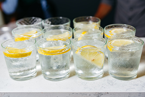 Multiple glasses of refreshing ice-cold lemon water garnished with lemon slices, ready to be served on a bar counter.