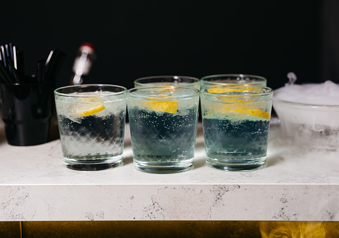Four mysterious smoky cocktails served on a marble bar counter, each garnished with a slice of lemon, in a dark atmospheric setting.