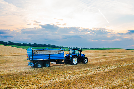 A blue tractor effortlessly pulls a blue trailer across a spacious field.