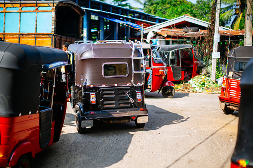 Tuk-tuks are lined up in a row, each with its unique design and vibrant colors. The middle tuk-tuk is prominently displayed, with its red and black color scheme and intricate design features.