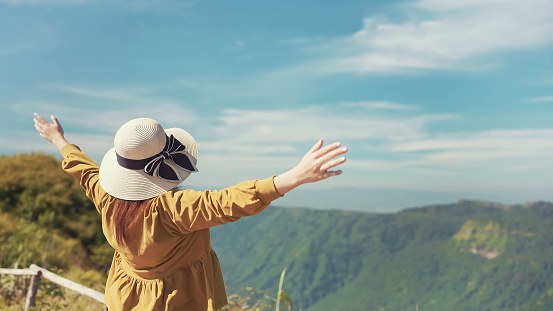 Rear view of happy woman traveler standing with raised hands relaxing while looking beautiful mountain view. Freedom, Travel lifestyle concept