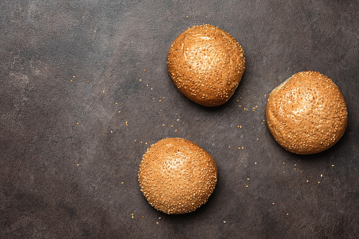 Fresh homemade buns with sesame seeds on a dark background. Top view, flat lay, copy space.