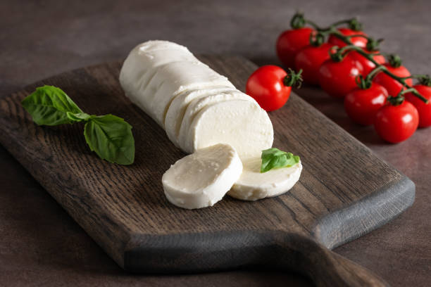 istock Mozzarella cheese sliced on a wooden cutting board with basil leaves and cherry tomatoes, side view, dark old background. 1927073049