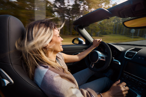 Young cheerful woman having fun while driving a convertible car in blurred motion.