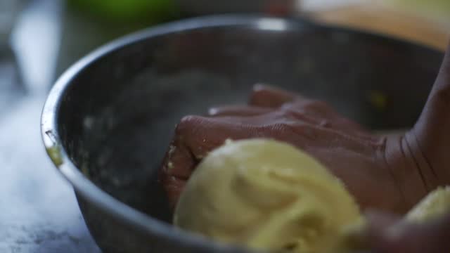 Wet and buttery dough mix being kneaded by hand in steel bowl, filmed as closeup slow motion shot
