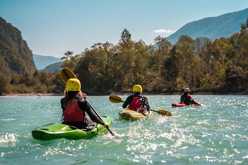 Kayakers of various ethnicities find tranquility as they navigate the gentle river currents near a verdant riverbank, enjoying the day's calm.