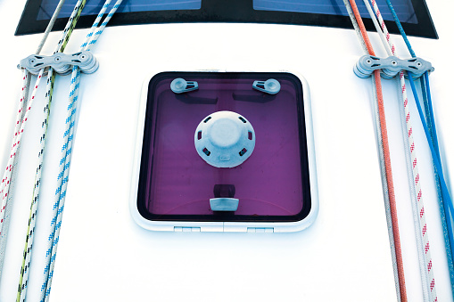 Part of the hull of a sailing yacht with multi-colored ropes, rollers, loops for securing sails, and a spare hatch to the yacht premises.