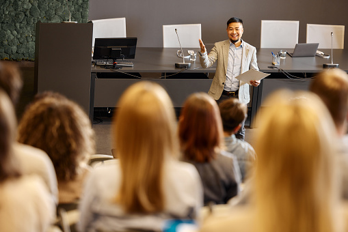 Male Teacher Giving a Lecture to a Diverse Multiethnic Group of Female and Male Students in Modern College Room. Curious and Thoughtful Scholars Studying and Listening to Lecturer. Camera Facing Class