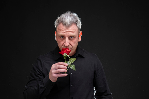 man holds in his hand a very pretty red rose that smells very subtle