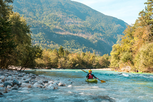 A young adult Caucasian female enjoys a solo kayaking trip, maneuvering through the turquoise waters of a serene river.