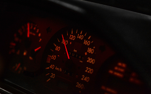 Speed limit. Dashboard of an old car with orange illuminated analog gauges and tachometer.